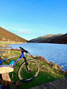 Pentland Cycle Hire bike leaning against bench overlooking a reservoir